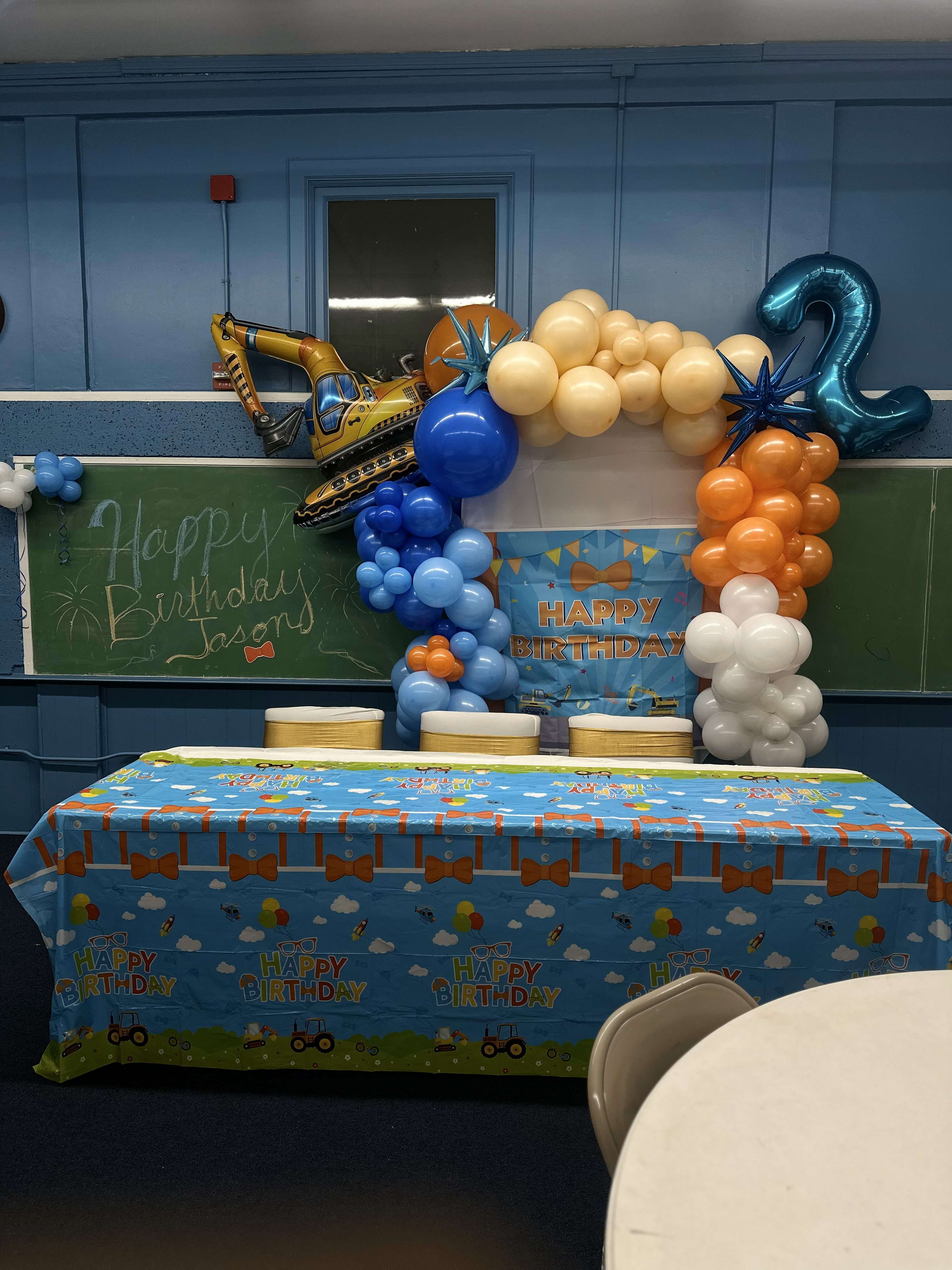 Celebrant with cake surrounded by family and blue and gold balloon clusters on stage.